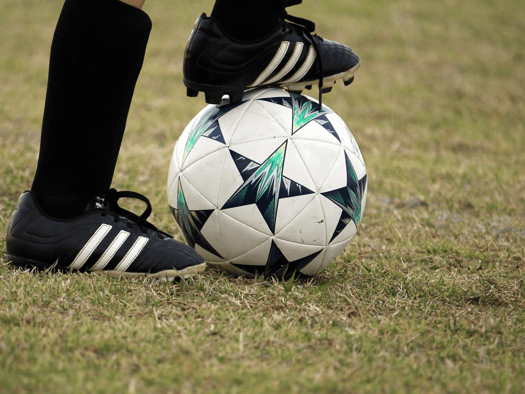 Close-up photo of cleat on top of soccer ball on the field.